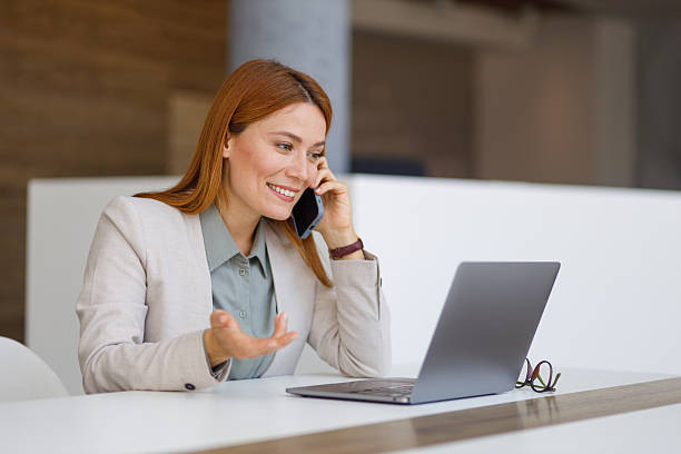 istock Smiling businesswoman talking on smartphone in office while working on laptop, managing multiple tasks efficiently 2249914997