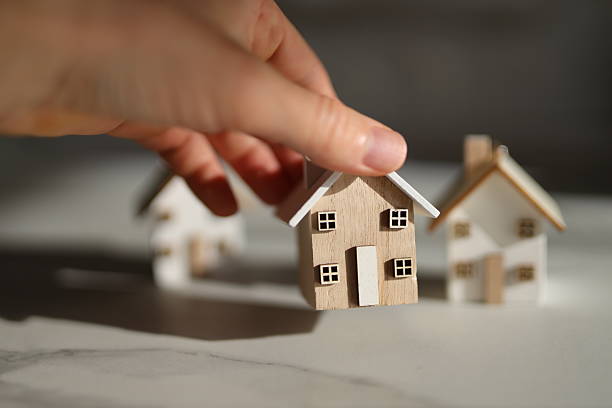 istock Hand placing wooden house model on table in sunlight 2249915429
