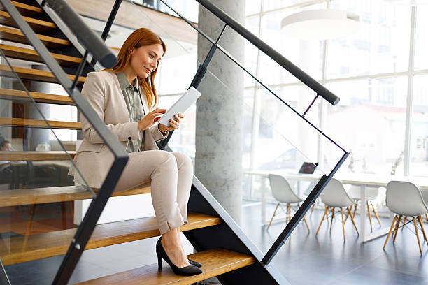 istock Businesswoman using digital tablet on office stairs, smiling and working with modern technology 2249915667