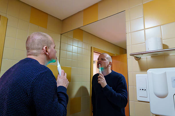 Man brushing teeth with electric toothbrush in bathroom