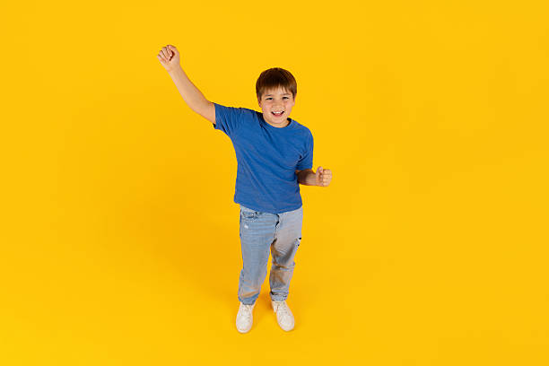 istock Preteen boy celebrating with raised hands in bright studio background 2249917764