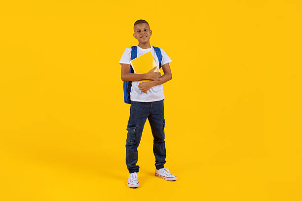 istock Preteen boy standing with notebook and backpack in bright yellow studio background 2249917911