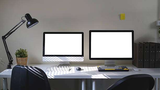 A workspace featuring a two computer monitor, desk lamp, and office supply elements.