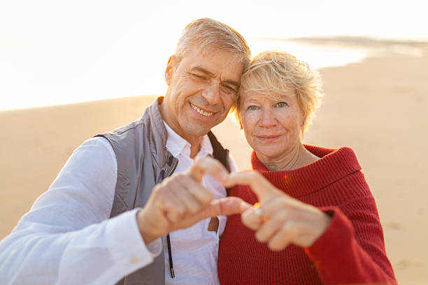 istock Happy senior couple creating heart hands gesture on beach 2249928872