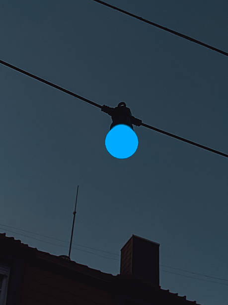Blue light bulb hanging from a wire against a twilight sky, illuminating the evening atmosphere with a soft glow, creating a serene and tranquil ambiance in urban settings