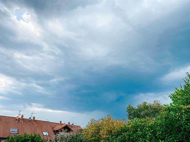 Dark clouds gather above rooftops and vibrant greenery, creating a dramatic atmosphere that evokes a sense of nature's power and beauty