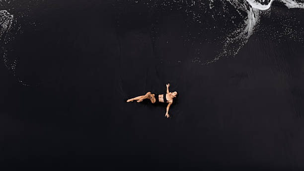 istock Woman relaxing on dark beach, surrounded by foamy waves 2249932704