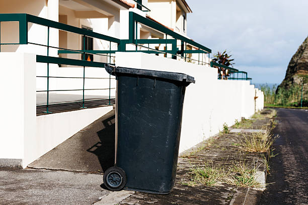 Black trash bin positioned on a residential street beside a white building, showcasing urban waste management and environmental care in a modern neighborhood setting