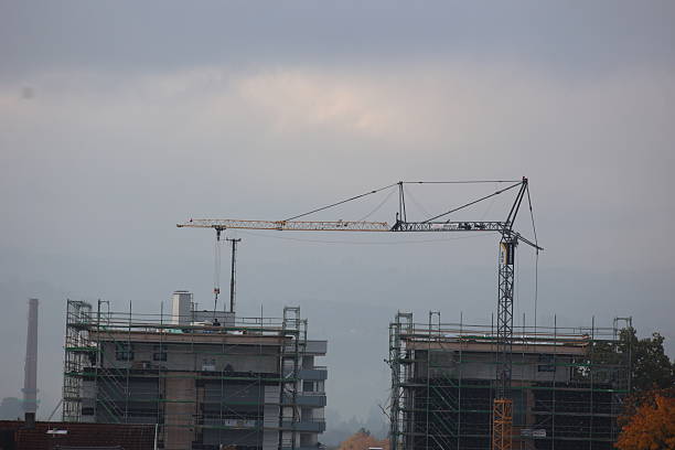 Crane is lifting a building in the distance. The sky is cloudy and the buildings are tall. .