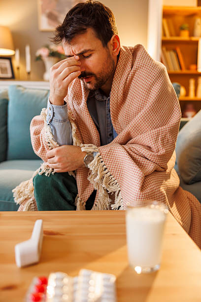 istock Sick man sitting on sofa wrapped in blanket having headache 2249935557