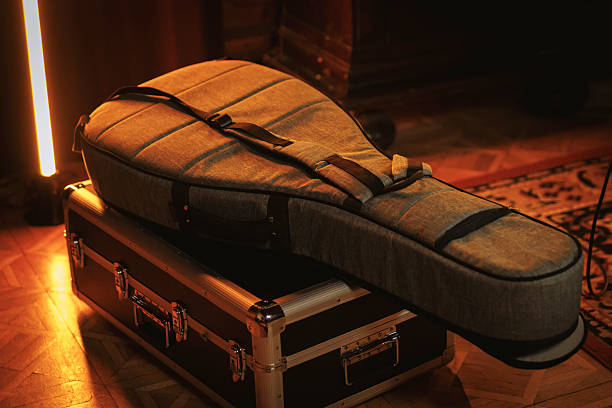 A padded guitar case lies on top of a metal flight case in a warmly lit room. The scene conveys preparation for a musical performance or rehearsal.
