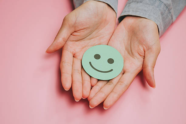 istock Smiling face icon on paper held by hands with pink background, symbolizing happiness and positive emotion in simple and warm composition 2249939010