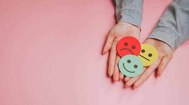 istock Emotional expression concept with hands holding colorful paper faces showing happy, neutral, and sad emotions on pink background, symbolizing mood and feelings 2249939030