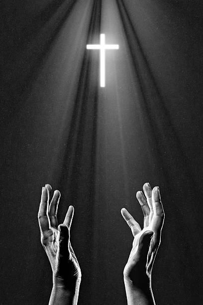 istock Hand Praying to Illuminated Cross in Black and White 2249939054