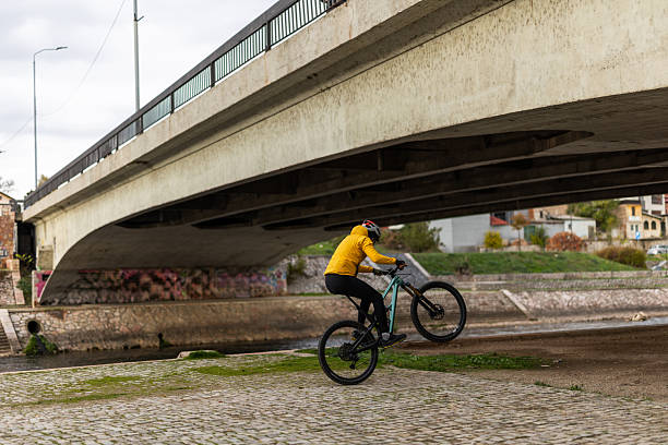 istock Cyclist Doing Wheelie Under Bridge in Urban Setting Wearing Bright Yellow Jacket During Daytime Outdoor Ride 2249939252
