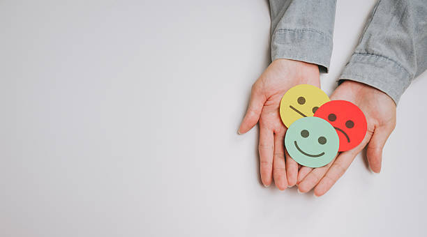istock Emotional expression concept with hands holding colorful paper faces showing happy, neutral, and sad feelings on white background 2249940026