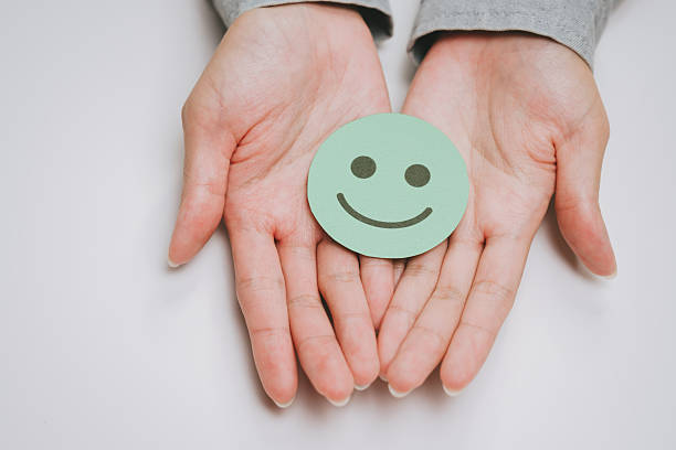 istock Smiling face icon on green paper held in open human hands symbolizing happiness and positivity with soft natural skin tone and neutral background 2249940035