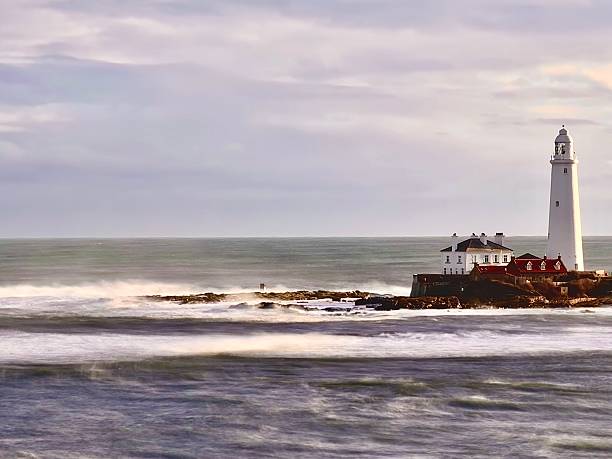St Mary’s Lighthouse against an overcast sky and breaking waves in long exposure