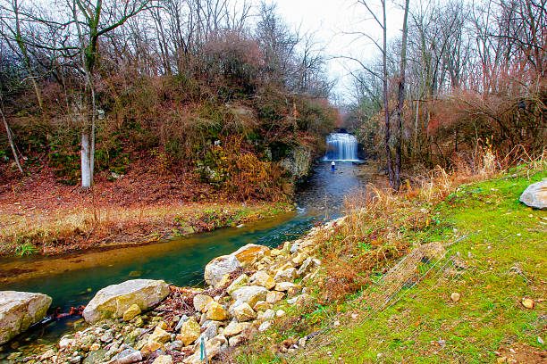 A waterfall flows into a cool pool of water that then winds through a canyon floor in the Midwest.  Matthiessen State Park in Illinois is a great place to view waterfalls and hike above and below the canyon walls.  While hiking to the waterfall a person can enjoy the cool weather inside the canyon while getting out of the sun.  The waterfall was highlighted by the light of the morning sun rising over the forest canopy.