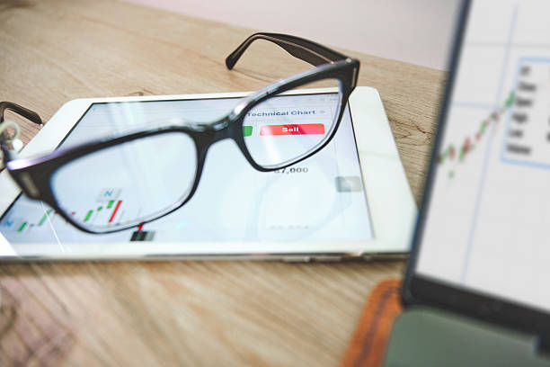 Eyeglasses resting on a tablet showing stock exchange charts and a sell button