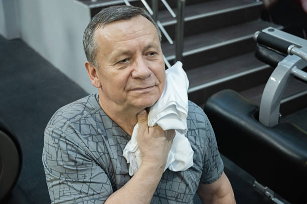 Adult man wipes sweat with a towel after training in a gym, showing post workout recovery and healthy lifestyle routine. Working Out in Gym
