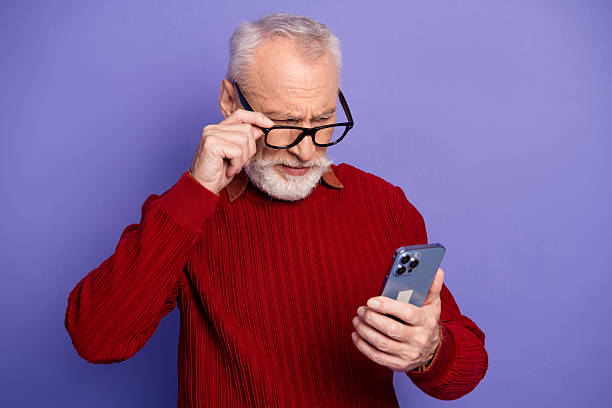 istock Elegant mature man in red sweater using smartphone in studio against purple background for lifestyle fashion and advertising 2249950423