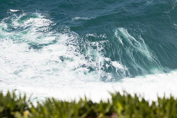 Dynamic ocean waves crashing against the shore, seen from above, with deep blue water and white foam creating a natural abstract pattern.