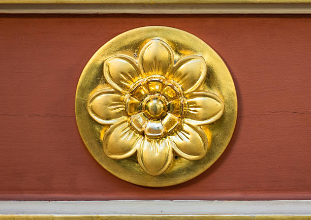 A polished gilded flower medallion is centered on a warm red wall, adding opulent decorative detail to architectural surfaces. The shiny finish conveys luxury, heritage, and craftsmanship
