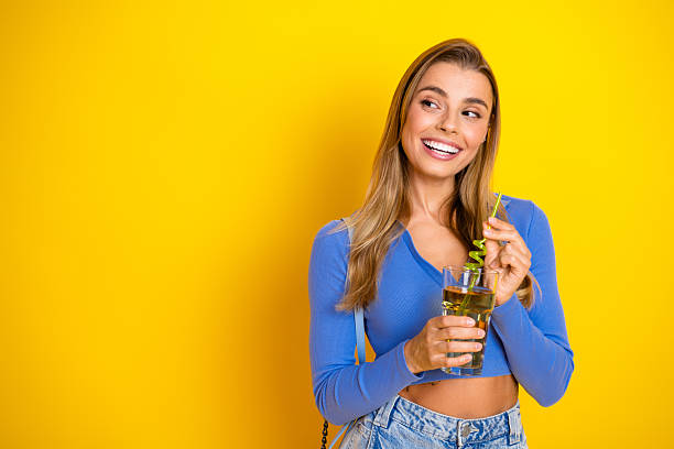 istock Young woman smiles while drinking a beverage with a straw against a bright yellow background for lifestyle fashion advertising and shopping 2249967699