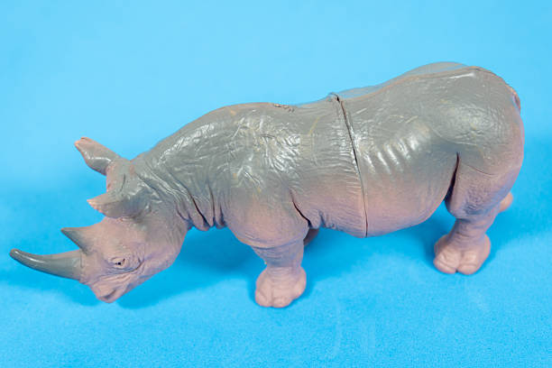 Close-up image of a toy rhinoceros figurine placed on a bright blue surface, featuring detailed textures and a realistic design.