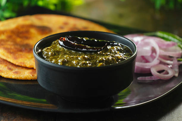 Traditional Punjabi sarson ka saag served with makki di roti, green chilies, onion slices, and fresh garnish.