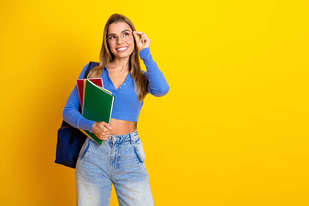 istock Young female student with notebooks and backpack smiles confidently against a bright yellow background wearing a blue top and jeans presenting fashion lifestyle education and youthful energy for advertising 2249970217