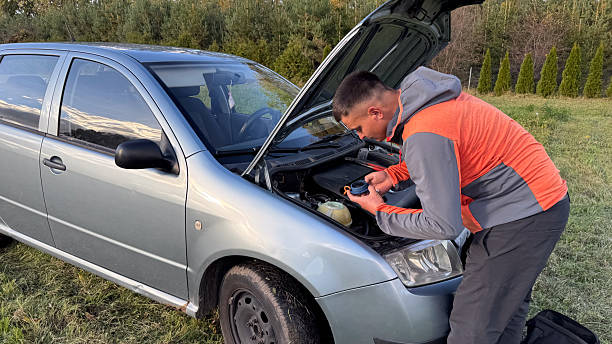 istock A man in a gray and orange jacket applies thread seal tape to a component while performing roadside car maintenance under the hood in a grassy field 2249971528