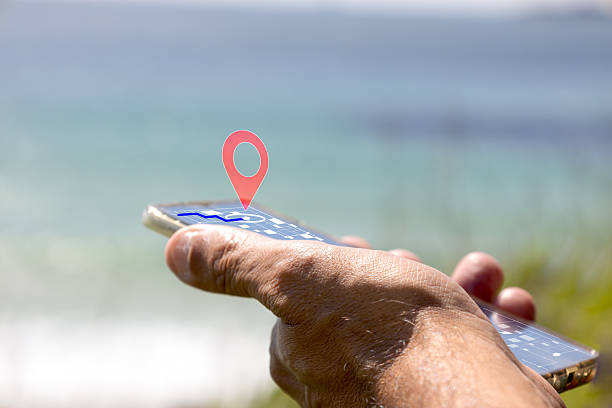 Person using a smartphone with a holographic location pin and navigation route overlay, finding a destination while enjoying the outdoors near a blue sea