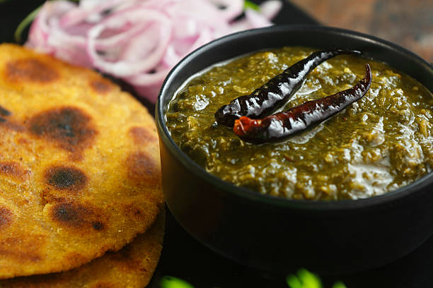Traditional Punjabi sarson ka saag served with makki di roti, green chilies, onion slices, and fresh garnish.