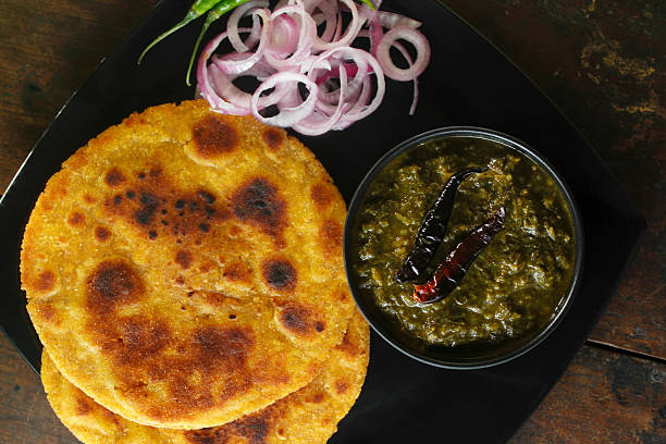 Traditional Punjabi sarson ka saag served with makki di roti, green chilies, onion slices, and fresh garnish.