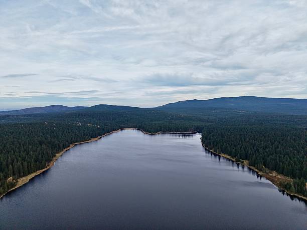 istock peaceful lake mirrors forest surroundings, tranquil water surface mirrors distant hills and sky 2249973846