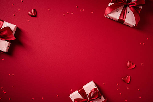 istock Happy Valentine's Day minimal background with pink gift boxes, hearts, and confetti on dark red table 2249980404