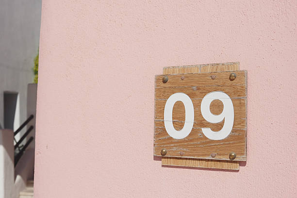 A wooden number 09 sign is mounted on a pale pink wall, showing clear detail.