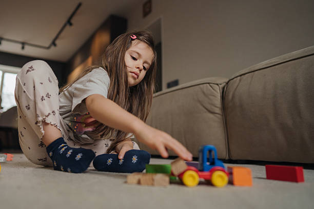 istock Child Mimics Driver, Young Girl Dressed Casually Explores Engineering Fun With Toy Car On Soft Carpet 2249981664