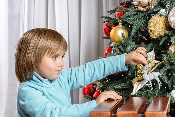Little boy holding a beautiful Christmas ornament, preparing to hang it on the tree. Bright festive scene on a yellow background, perfect for holiday ads, cards and seasonal designs.