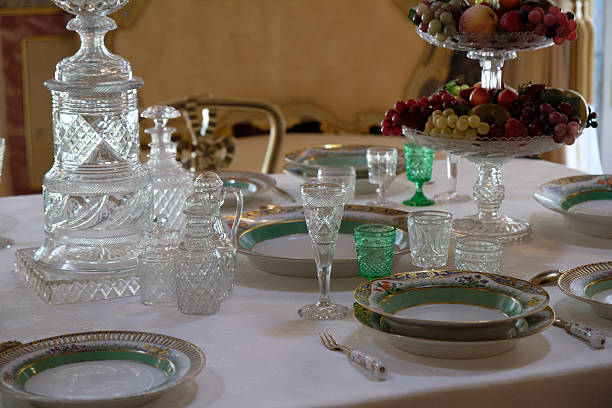 A table is set with plates, glasses, and a fruit bowl during a gathering. The light filters through large windows, creating a bright atmosphere in the room.
