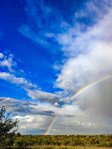 istock Bright rainbow arches above green fields and village roofs after rain. Dramatic sky, vivid colors and weather concept. 2249985594