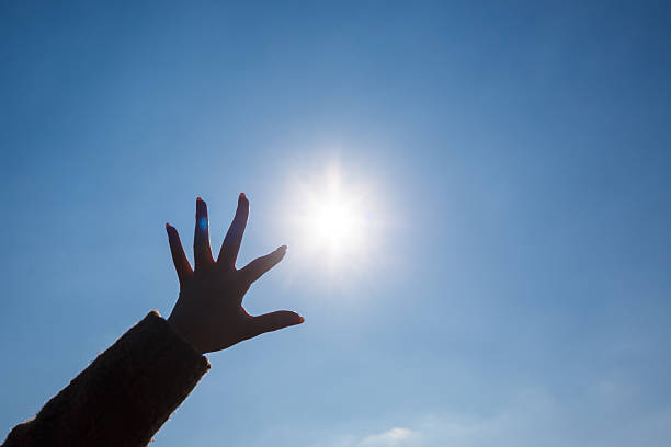 istock silhouetted a female hand against a blue sky and bright sun 2249986219