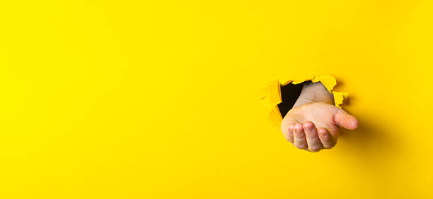 istock Hand emerging from a torn yellow wall, symbolizing creativity and breaking barriers in design 2249987188