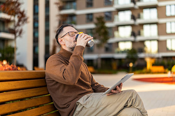 Handsome mid adult man checking a message on a digital touch panel end enjoying in the autumn sunny day while sipping coffee. Technology and working online concept.