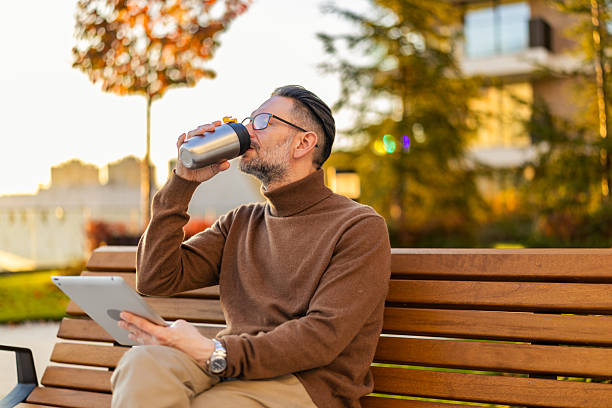Handsome mid adult man checking a message on a digital touch panel end enjoying in the autumn sunny day while sipping coffee. Technology and working online concept.