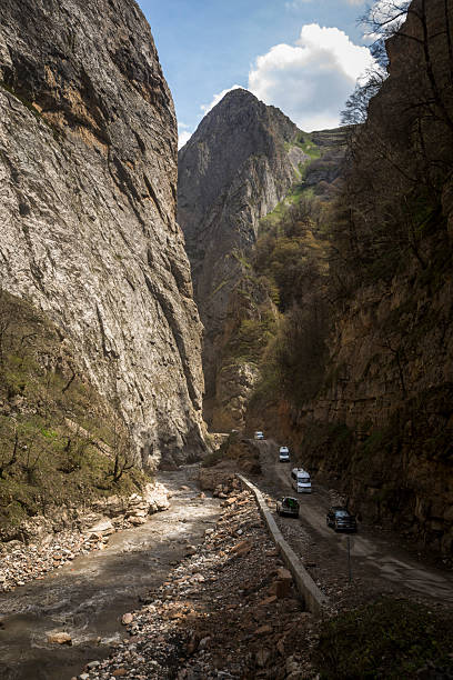 Vehicles drive beside river through steep mountains, Greater Caucasus Mountains