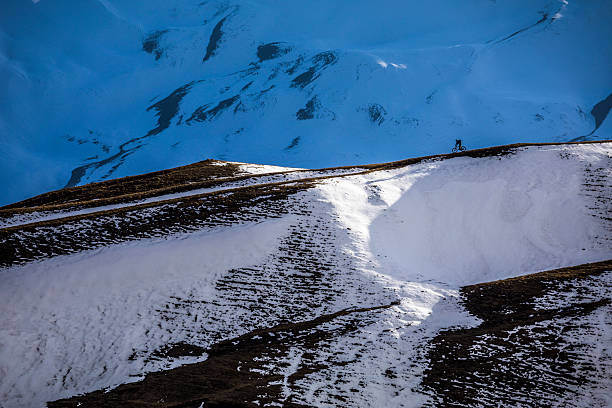 Distant view of mountain biker rides on alpine slope, snowcapped mountains, Greater Caucasus Mountains