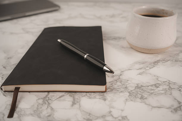 istock A black notebook lies open on a smooth marble surface, accompanied by a sleek silver pen. This serene setting invites creativity and thoughtful writing at any time 2250001790